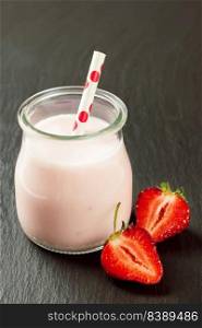 Strawberry milkshake in the glass jar with drinking straw on black slate background. vertical photo. Strawberry milkshake in the glass jar on black slate background