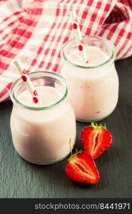 Strawberry milkshake in the glass jar with drinking straw on black slate background. vertical photo. Strawberry milkshake in the glass jar on black slate background