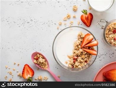 Strawberry organic granola with milk and pink spoon on light kitchen board. Top view.