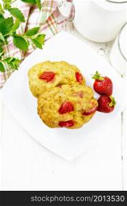 Strawberry scones in a plate with berries, a towel, mint, milk in jug and glass on wooden board background from above