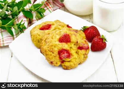 Strawberry scones in a plate with berries, a towel, mint, milk in jug and glass on the background of light wooden board