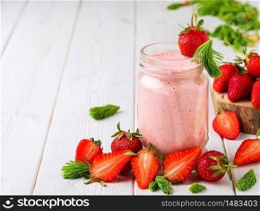 Strawberry smoothie in a glass jar on a wooden white table. Strawberries and spruce tips, smoothie ingredients scattered on the table. Close-up with copy space.. Strawberry cocktail in a glass jar on a wooden white table. Strawberries and spruce tips, smoothie ingredients scattered on the table. Close-up with copy space.