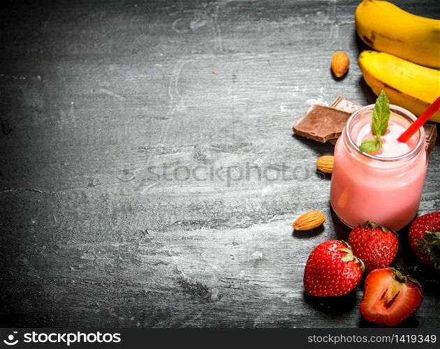 Strawberry smoothie with berries, chocolate, nuts and bananas. On the black wooden table.. Strawberry smoothie with berries, chocolate, nuts and bananas.