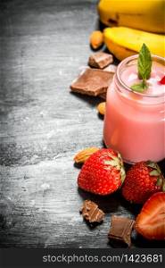 Strawberry smoothie with berries, chocolate, nuts and bananas. On the black wooden table.. Strawberry smoothie with berries, chocolate, nuts and bananas.