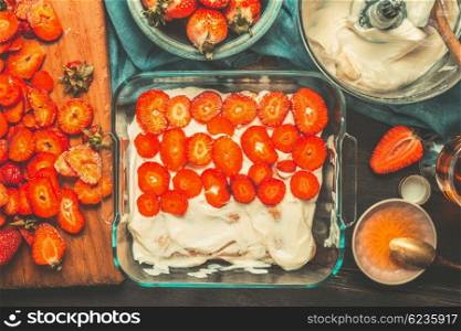 Strawberry tiramisu cake preparation with sliced Strawberries on dark rustic kitchen table , top view. Italian food concept