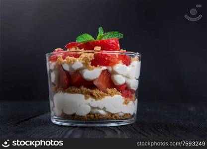 Strawberry with cookie and cream dessert decorated with mint leaf on black wooden background. Strawberry with cookie and cream dessert