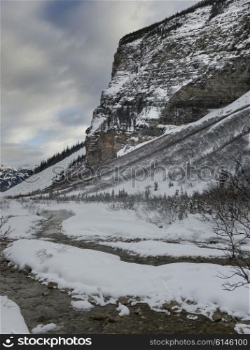 Stream flowing in snow covered valley in winter, Lake Louise, Banff National Park, Alberta, Canada