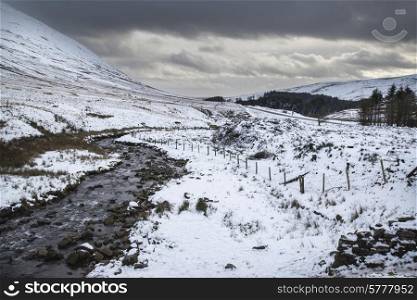 Stream flowing through snow covered Winter landscape in mountains