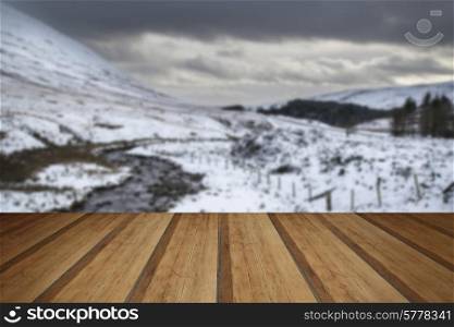 Stream flowing through snow covered Winter landscape in mountains with wooden planks floor