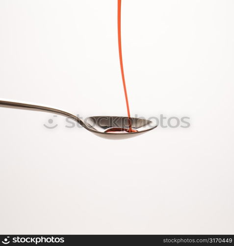 Stream of red cough syrup being poured into spoon.