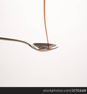 Stream of red cough syrup being poured into spoon.