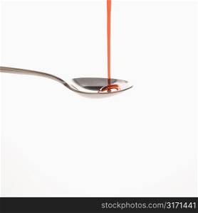 Stream of red cough syrup being poured into spoon.