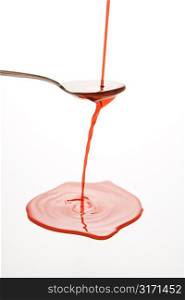 Stream of red cough syrup overflowing spoon into puddle below.