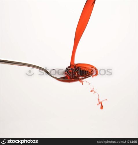 Stream of red cough syrup splashing out of spoon.