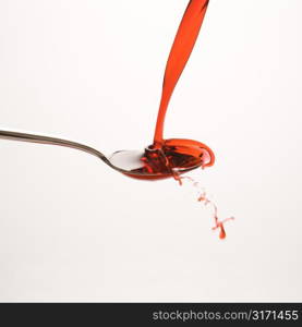 Stream of red cough syrup splashing out of spoon.