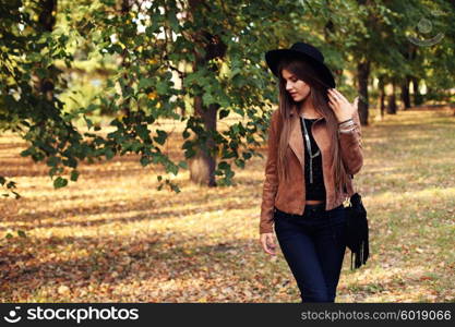 Street fashion concept - closeup portrait of a pretty girl. Wearing hat and suede jacket holding bag with fringe. Beautiful autumn woman.