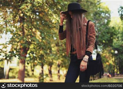 Street fashion concept - closeup portrait of a pretty girl. Wearing hat and suede jacket holding bag with fringe. Beautiful autumn woman.