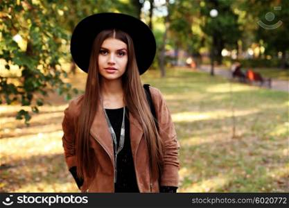 Street fashion concept - closeup portrait of a pretty girl. Wearing hat and suede jacket holding bag with fringe. Beautiful autumn woman.