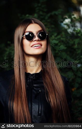 Street fashion concept - closeup portrait of a pretty girl. Wearing leather jacket, round sunglasses. Autumn woman. Artsy bohemian rock style. Fall fashion.