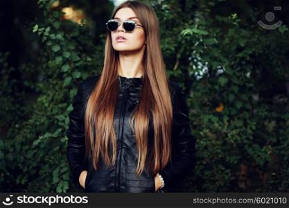 Street fashion concept - closeup portrait of a pretty girl. Wearing leather jacket, round sunglasses.