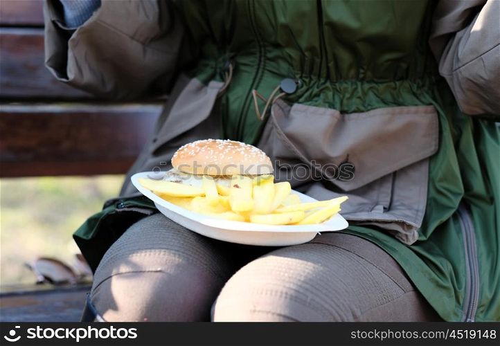 Street food. Woman holding hamburger and french fries outdoors.