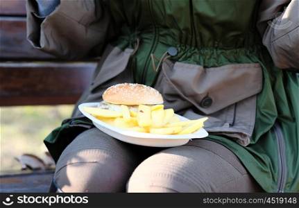 Street food. Woman holding hamburger and french fries outdoors.