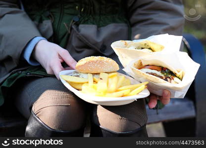 Street food. Woman holding hamburgers and french fries outdoors.