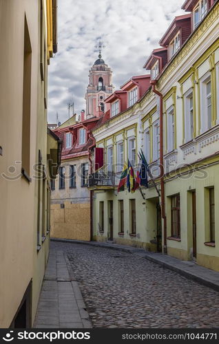 Street of the old city, the picturesque old houses with flags over the entrance and the bell tower of the Catholic church of All Saints. Vilnius. Lithuania