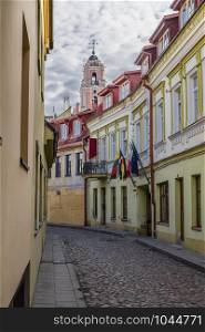 Street of the old city, the picturesque old houses with flags over the entrance and the bell tower of the Catholic church of All Saints. Vilnius. Lithuania