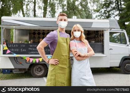 street sale and people concept - couple of young sellers wearing face protective medical mask for protection from virus disease at food truck. couple of young sellers in masks at food truck