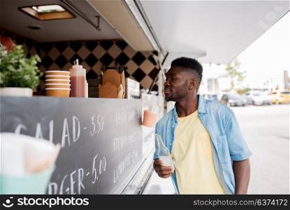 street sale and people concept - happy african american young man with drink at food truck. african american man with drink at food truck