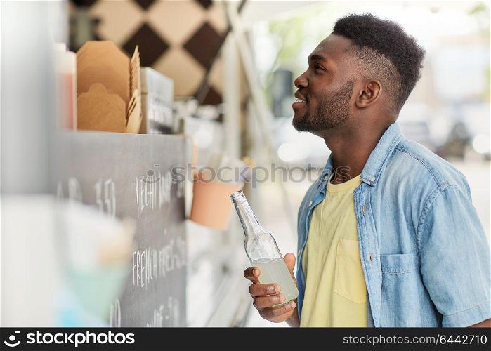 street sale and people concept - happy african american young man with drink at food truck. african american man with drink at food truck