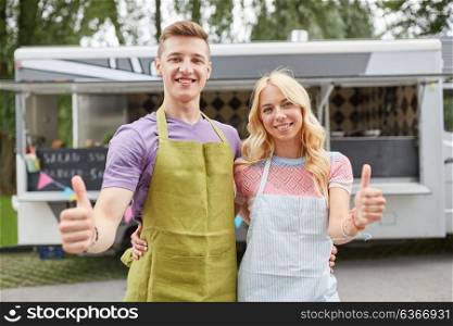 street sale and people concept - happy couple of young sellers at food truck showing thumbs up. couple of sellers at food truck showing thumbs up