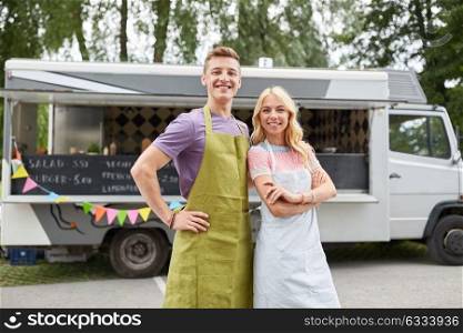 street sale and people concept - happy couple of young sellers at food truck. happy couple of young sellers at food truck