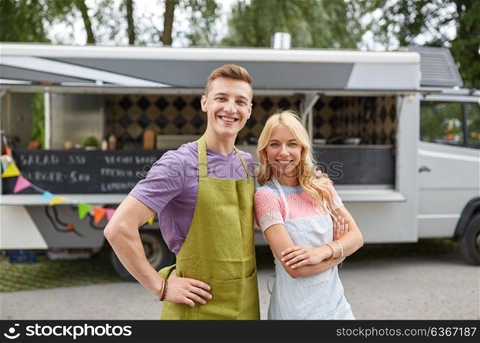 street sale and people concept - happy couple of young sellers at food truck. happy couple of young sellers at food truck