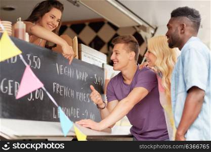 street sale and people concept - happy customers or friends looking at billboard at food truck. happy customers or friends at food truck