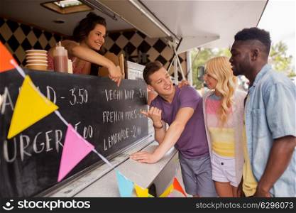 street sale and people concept - happy seller showing menu to customers or friends at food truck. seller showing menu to customers at food truck