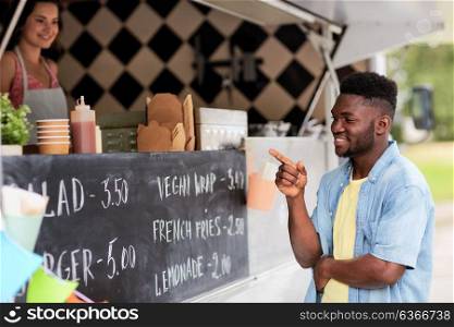 street sale and people concept - happy smiling male customer looking at billboard at food truck. male customer looking at billboard at food truck