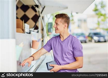 street sale and people concept - happy young male customer with wallet making order at food truck. male customer with wallet at food truck