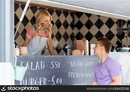 street sale and people concept - happy young saleswoman at food truck serving male customer. saleswoman at food truck serving male customer