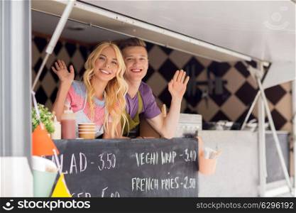 street sale and people concept - happy young sellers waving hands and greeting at food truck. happy young sellers waving hands at food truck