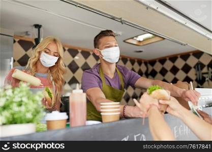 street sale and people concept - young sellers wearing face protective medical mask for protection from virus disease serving customers at food truck. sellers in masks serving customers at food truck