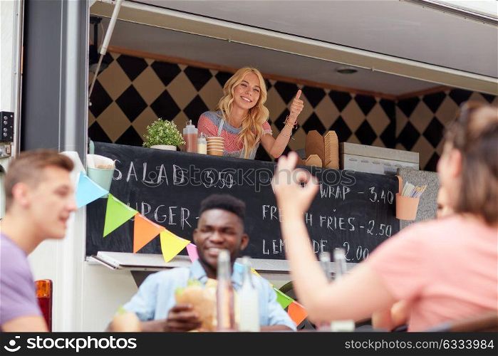 street sale, customer service and people concept - happy saleswoman at food truck showing thumbs up. happy saleswoman showing thumbs up at food truck