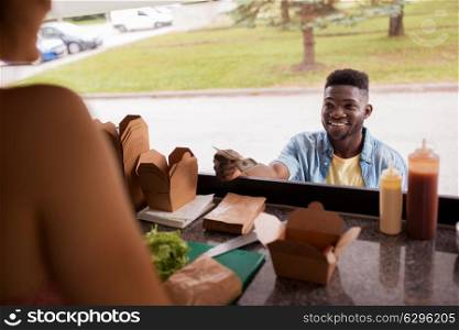 street sale, payment and people concept - happy african american young man buying wok and paying with dollar money at food truck. african american man buying wok at food truck