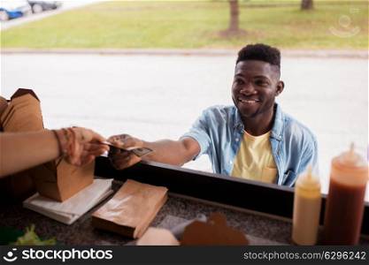 street sale, payment and people concept - happy african american young man buying wok and paying with dollar money at food truck. african american man buying wok at food truck