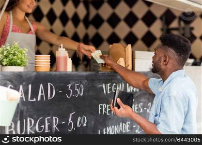 street sale, payment and people concept - happy african american young man paying money to saleswoman at food truck. african american man paying money at food truck