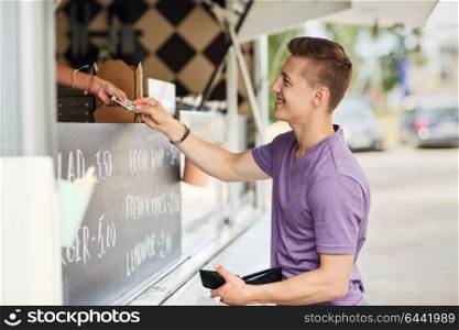 street sale, payment and people concept - happy young man paying money at food truck. happy young man paying money at food truck