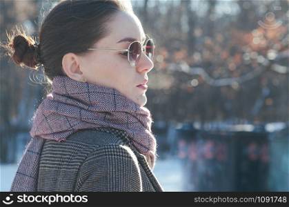 Street style Fashion portrait charming young woman in trendy casual clothes, in park. Brown overcoat, light red scarf, sun glasses. Winter collection Classic look
