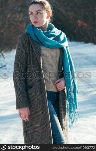 Street style Fashion portrait charming young woman in trendy casual clothes, in snowy park. Pullover, brown overcoat, blue jeans and scarf. Sunny winter day, city lifestyle. Classic look, motion blur