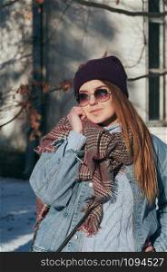 Street style Fashion portrait pretty young girl in trendy casual clothes, smiling, in sun glasses. Sunny winter day, city lifestyle